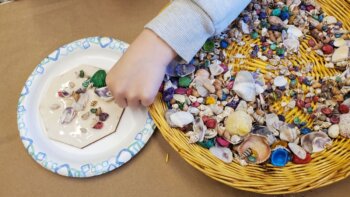 Child's hand glues seashells to a board.