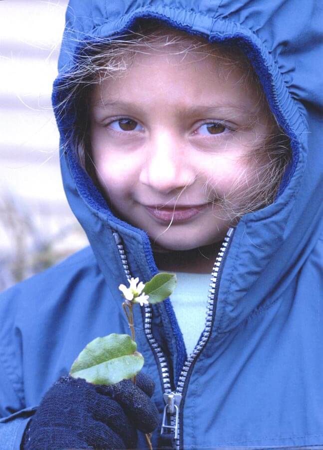 Young girl in blue jacket holding a mayflower.